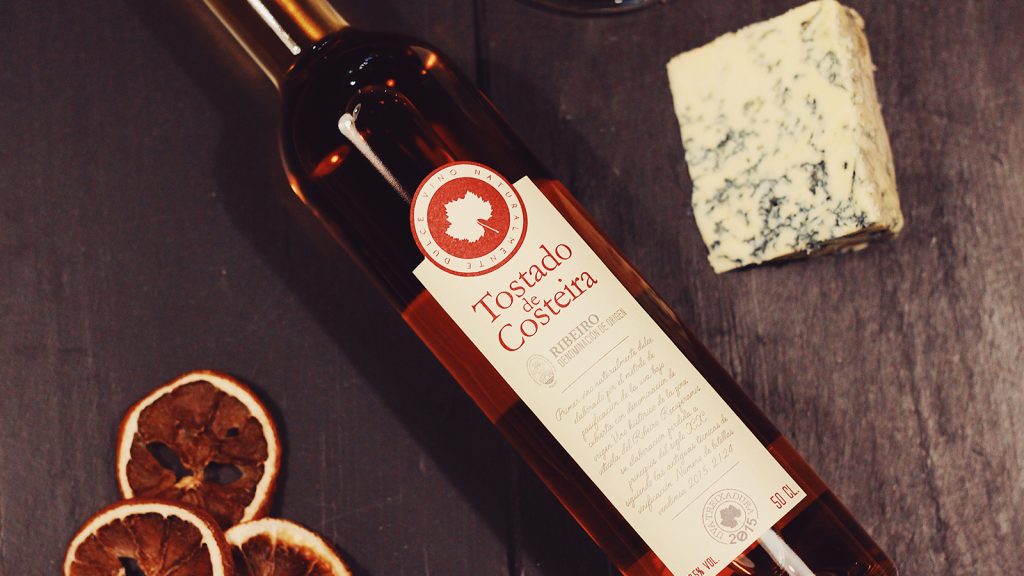 Botella de vino Tostado de Costeira Ribeiro acompañada de queso azul y rodajas de naranja deshidratada, presentación gourmet sobre mesa oscura.