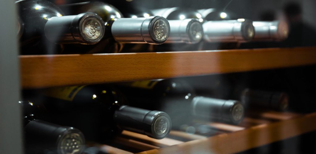 Conservar vino en casa con una vinoteca o nevera de vinos climatizada. Botellas de vino tinto y blanco almacenadas en posición horizontal.